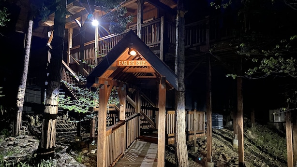 Una cabaña de madera con una escalera de madera que lleva a una terraza, rodeada de árboles.