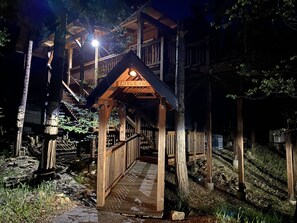 Eine Holzhütte mit einer Holztreppe, die zu einer Terrassenfläche führt, umgeben von Bäumen.