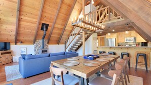 Un loft spacieux avec un plafond haut, une table à manger en bois avec des chaises, un canapé bleu et un coin cuisine équipé d’appareils électroménagers modernes.