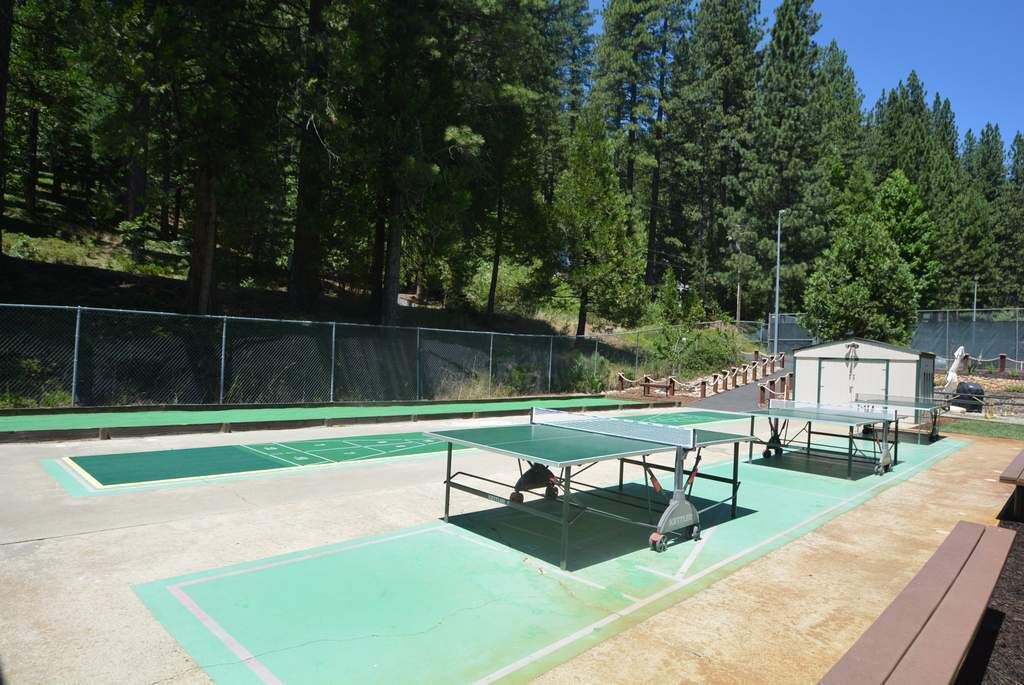 Un court de tennis en plein air, doté d’un filet, entouré d’une clôture et d’arbres.