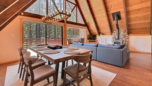 Un loft spacieux avec un plafond haut, un coin repas avec une table et des chaises en bois, un canapé gris et une cheminée en pierre.