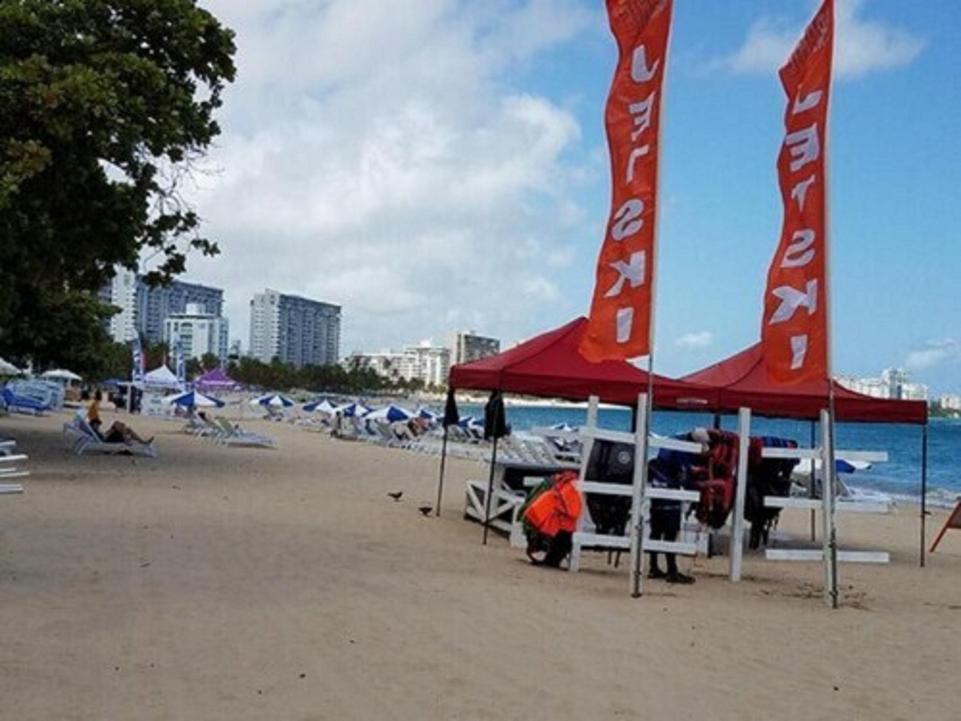 Una playa con tiendas de campaña rojas y una persona con una chaqueta naranja.