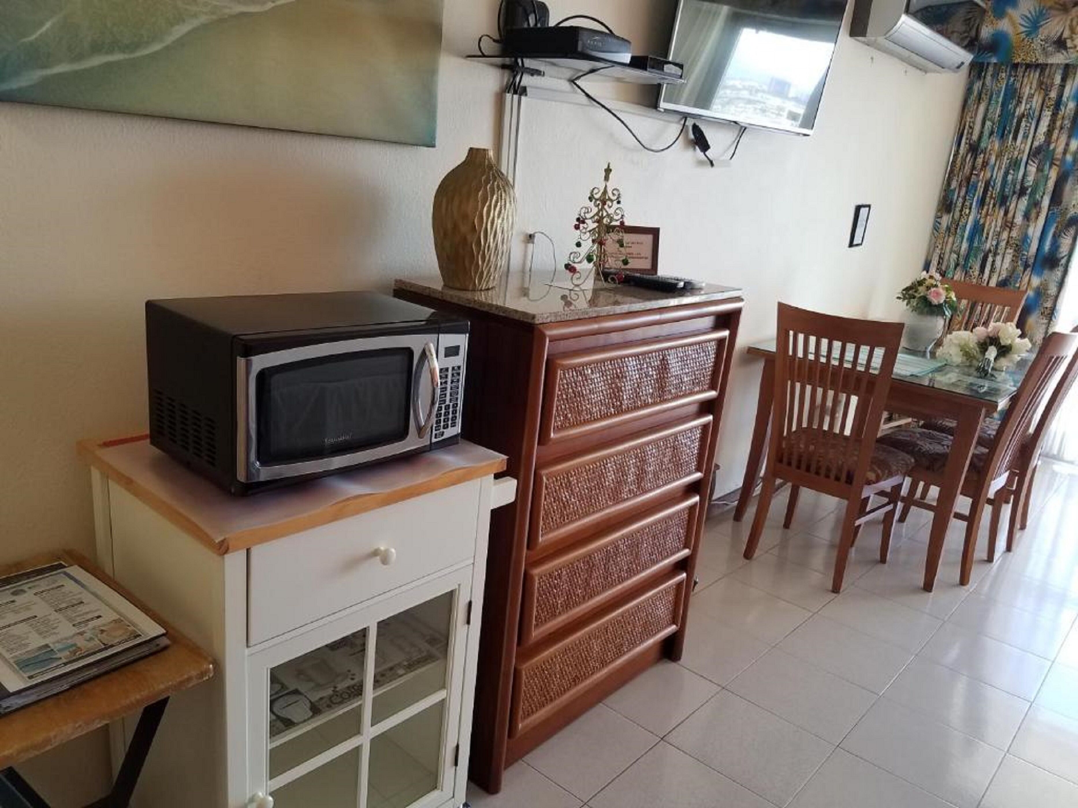 Une cuisine compacte avec un micro-ondes posé sur un meuble en bois, un petit réfrigérateur et un coin repas comprenant des chaises et une table.