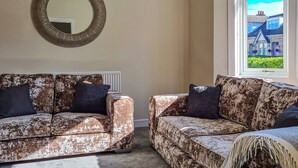 Ein Wohnzimmer mit zwei gestreiften Sofas, einem runden Spiegel und einem Fenster mit Blick auf Häuser.