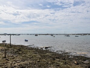 A coastal scene with boats on calm waters, rocky shore, and a distant shoreline with buildings.