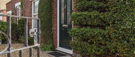 A brick house with a dark green door, a small garden with gravel, and a metal gate.
