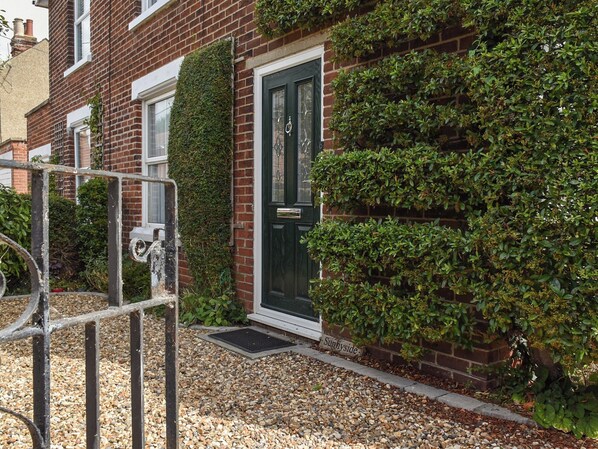 A brick house with a dark green door, a small garden with gravel, and a metal gate.
