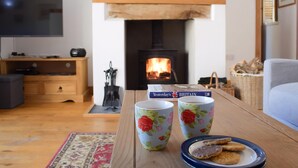 A cozy living room with a fireplace, a television, and a coffee table with floral mugs and biscuits.
