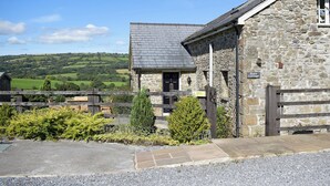 A stone cottage with a sloped roof, a wooden fence, and a view of rolling hills.