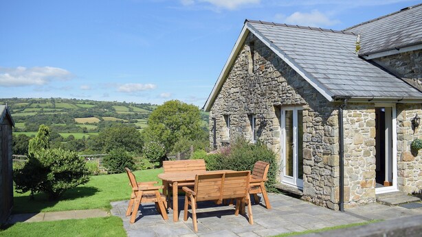 A stone building with a sloped roof and a patio with wooden furniture.