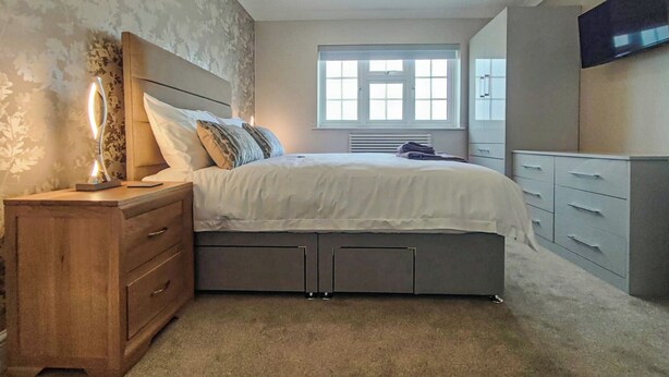 Ein Schlafzimmer mit Bett, Nachttisch, Lampe, Kleiderschrank und einem an der Wand montierten Fernseher.