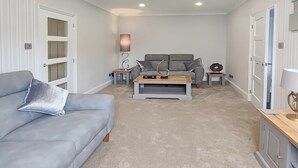 Ein Wohnzimmer mit grauem Sofa, Couchtisch und grauem Sessel. Zwei Beistelltische mit Dekorationselementen.