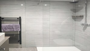 Ein modernes Badezimmer mit Duschkabine aus Glas, einer weißen Badewanne und einem Handtuchhalter mit einem violetten Handtuch.