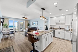 A modern kitchen with white cabinets, a central island, and a dining area with a view of the ocean.