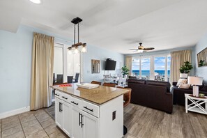 A modern kitchen with a central island, a dining area with chairs, a sofa, and a ceiling fan.