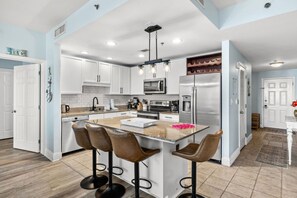 A modern kitchen with white cabinets, a granite countertop, a central island with bar stools, and stainless steel appliances.