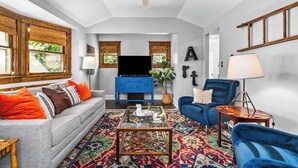 A spacious living room with a large TV, blue furniture, and a ceiling fan. - Spacious Home in KC's Core 46 (Kansas City)