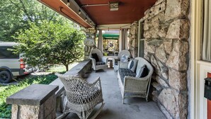 A covered porch with stone walls, wicker furniture, and a vehicle parked outside. - Spacious Home in KC's Core 46 (Kansas City)