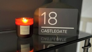 Une bougie portant l’étiquette « RESTORE » et une bouteille avec l’inscription « 18 CASTLEGATE » sur une surface réfléchissante.