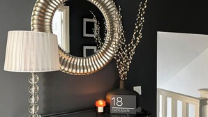 Un intérieur moderne avec un mur noir, un miroir décoratif, un radiateur blanc et une étagère noire sur laquelle sont posés une bougie et un panneau indiquant « 18 CASTLEGATE ».