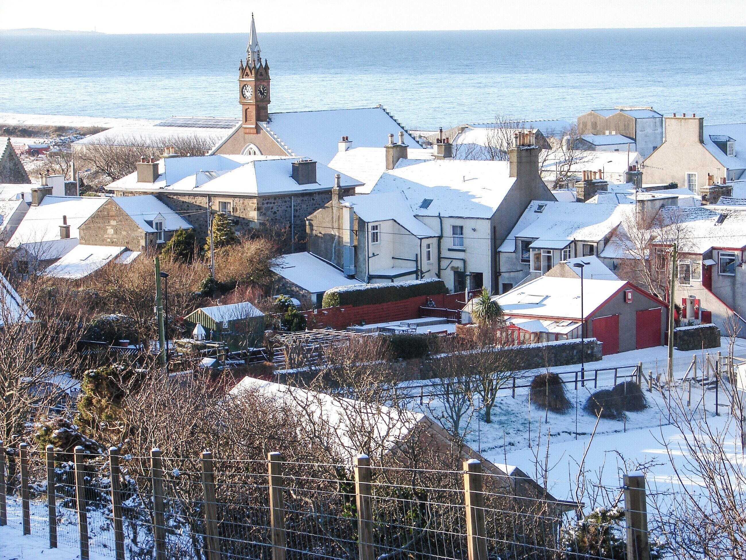 A coastal town with snow-covered buildings and a prominent church tower.