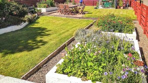 A well-maintained garden with a lawn, flower beds, and a wooden deck. - A perfect coastal escape for couples and friends. (Ballantrae)