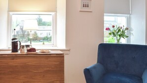 A room with a wooden desk, a blue armchair, and a window with a view of a garden. - A perfect coastal escape for couples and friends. (Ballantrae)