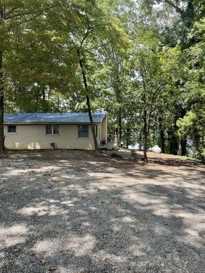 A single-story house with a metal roof, surrounded by trees and a gravel driveway.