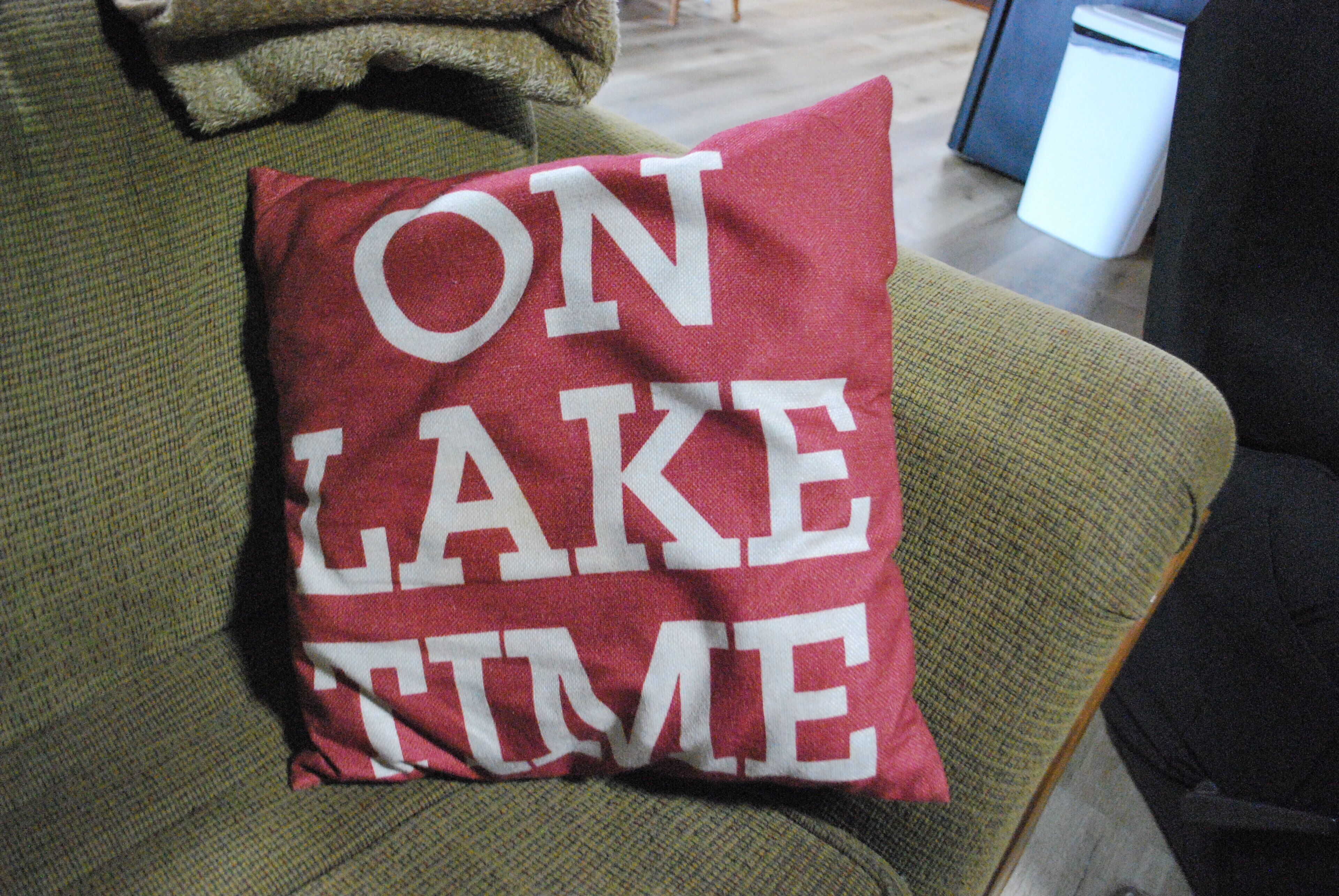 Vihreällä sohalla on koristetyyny, jossa lukee teksti: ”ON LAKE TIME”.