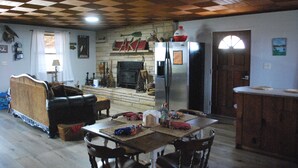 A cozy living room with a fireplace, a dining area with a table and chairs, and a kitchen area with a refrigerator. - Weiss Lake Rustic Cabin on the water, new flooring! (Centre)