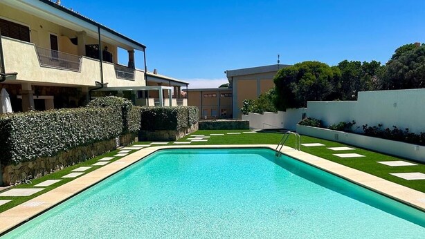 A rectangular swimming pool with a wooden deck in the foreground, surrounded by a well-maintained lawn and a hedge. - stunning aparment with private pool - 5 min from the beach (Palau)