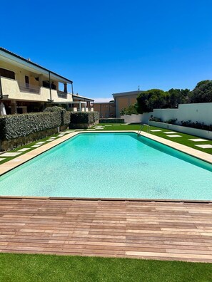 A rectangular swimming pool with a wooden deck in the foreground, surrounded by a well-maintained lawn and a hedge. - stunning aparment with private pool - 5 min from the beach (Palau)