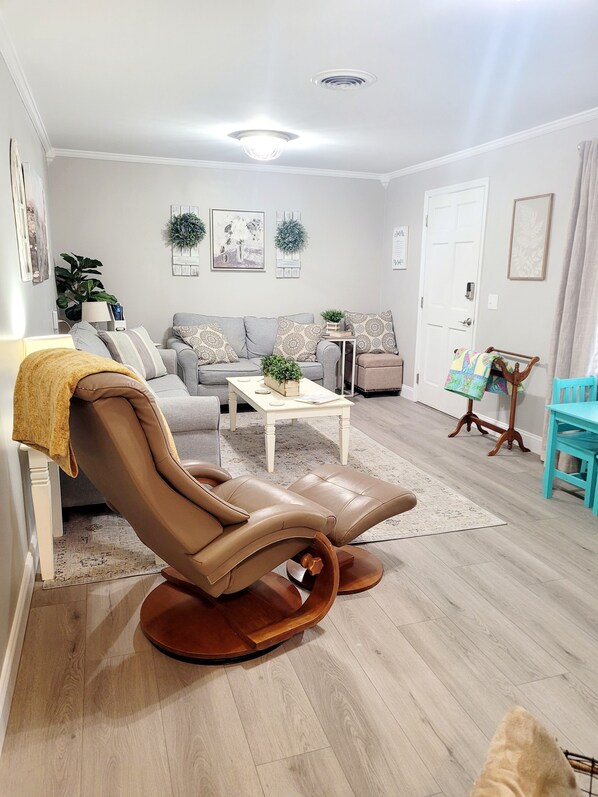 A modern living room with a leather recliner, a grey sofa, a white coffee table, and a blue chair.
