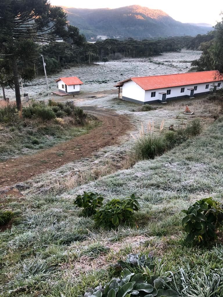 A rural landscape with a dirt path leading to a white building with a red roof.