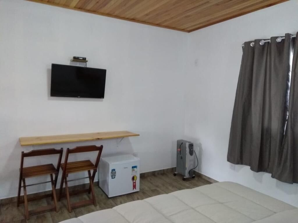Una habitación con cama, un escritorio y dos sillas, un televisor montado en la pared, un calefactor y una cortina.