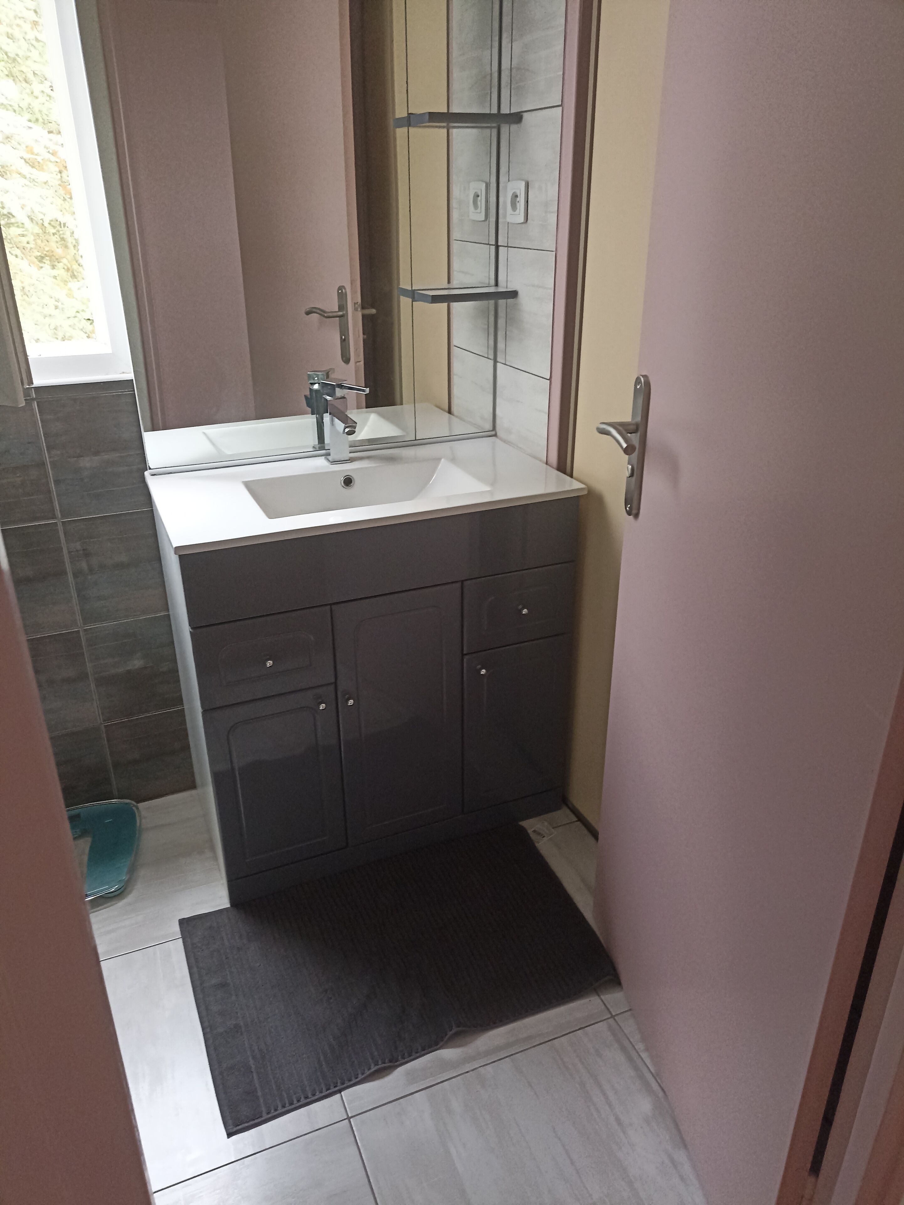 Een badkamer met een witte wastafel, donkere kastjes en een spiegel.