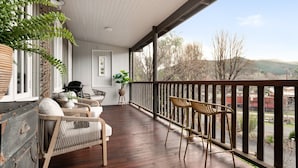 A covered porch with wicker furniture, a grill, and a view of a train and hills. - Eliza's Bright (Bright)