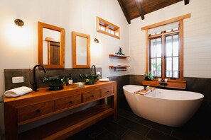 Une salle de bain moderne avec un meuble-lavabo en bois, deux bols en verre vert, une baignoire sur pieds et une fenêtre avec des cadres en bois.