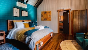A bedroom with a wooden bed, a blue wall, a wooden floor, a blue armchair, and a door leading to another room. - Eliza's Bright (Bright)