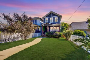 A two-story house with a front porch, a white picket fence, and a well-maintained lawn. - Southern Craftsman · Front Porch · Fenced Yard · Patio · Walk to Five Points (Nashville)