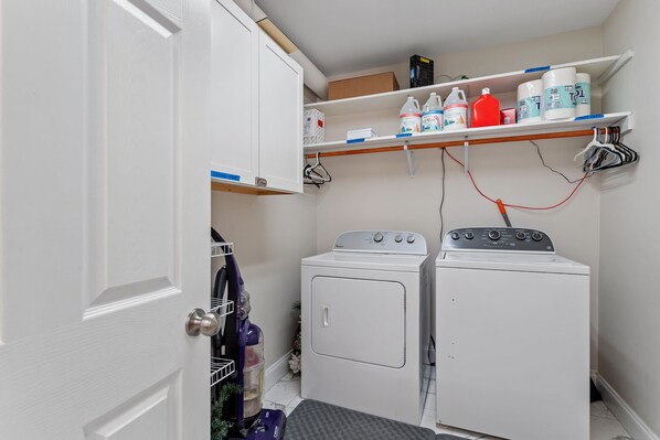 A laundry area with a washing machine, dryer, and shelves with cleaning supplies.