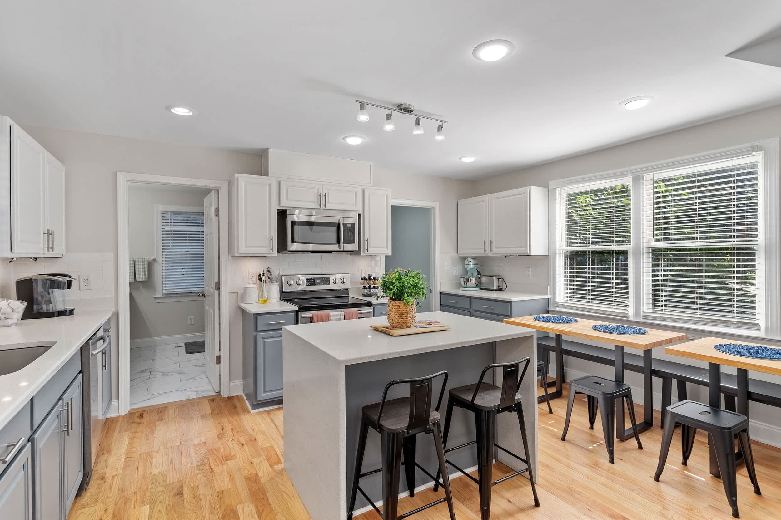 A modern kitchen with white cabinets, a central island with stools, a microwave, and a coffee maker.