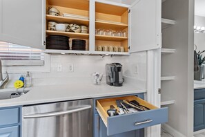 Una cocina con armarios blancos, un refrigerador de acero inoxidable, una cafetera y un cajón con utensilios.