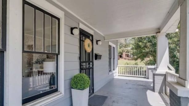 A covered porch with a white railing, a black gate, and a wreath on the door. - Downtown Raleigh: Spacious, Pet-Friendly, Fenced (Raleigh)