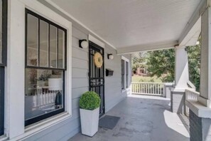 A covered porch with a white railing, a black gate, and a wreath on the door. - Downtown Raleigh: Spacious, Pet-Friendly, Fenced (Raleigh)