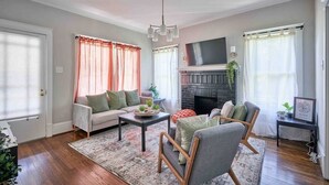 A living room with a fireplace, sofa, armchair, and coffee table. - Downtown Raleigh: Spacious, Pet-Friendly, Fenced (Raleigh)