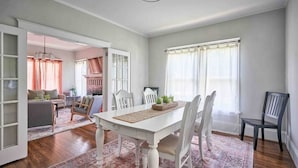 A dining area with a white table, chairs, and a rug. There is a kitchen in the background with a brick wall and a window with curtains. - Downtown Raleigh: Spacious, Pet-Friendly, Fenced (Raleigh)
