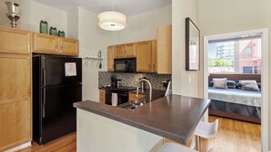 A modern kitchen with wooden cabinets, a black refrigerator, a microwave, and a sink. - Warehouse District Modern Condo w/ Private Garage (Raleigh)