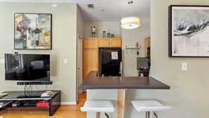 A modern kitchen with a central island, a built-in oven, and a refrigerator. There is a dining area with a bar counter and two stools. - Warehouse District Modern Condo w/ Private Garage (Raleigh)