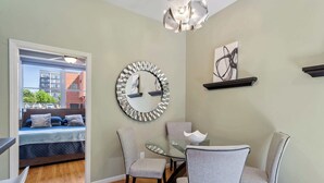 A modern dining area with a glass table, grey upholstered chairs, and a decorative mirror on the wall. - Warehouse District Modern Condo w/ Private Garage (Raleigh)